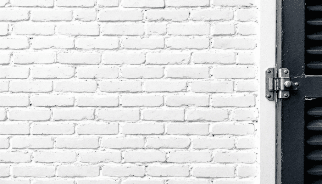 Closeup White Wall - Ranch Style Homes USA The image features a close-up view of a white painted brick texture, showcasing the smooth surface and subtle variations in color. Black window shutters and hardware details add a modern contrast, enhancing the character of this white brick ranch home.