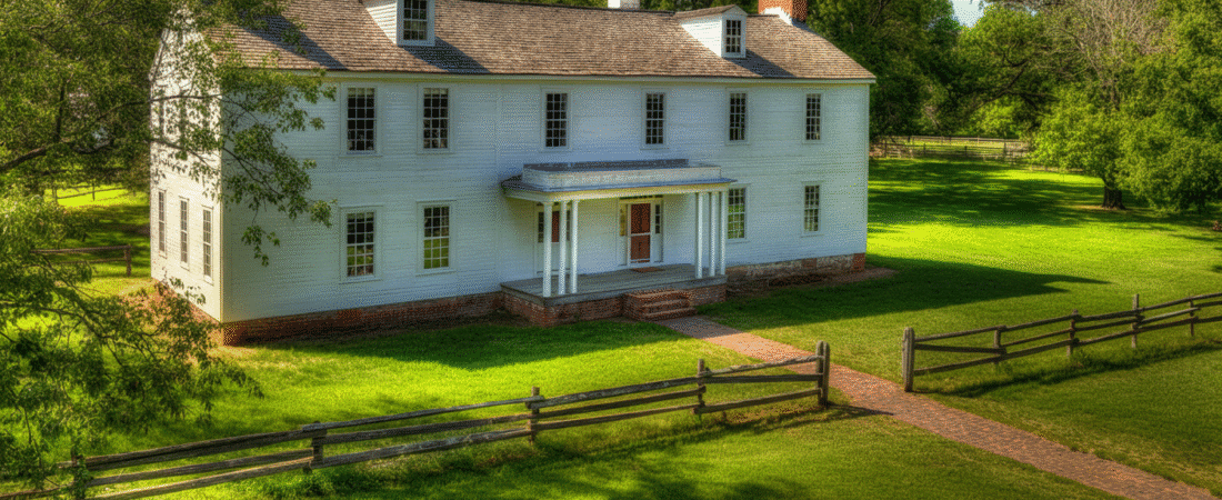 Photograph of a charming historic white colonial-style house with a red door, surrounded by lush green lawns and mature trees under a bright blue sky, evoking tranquility.