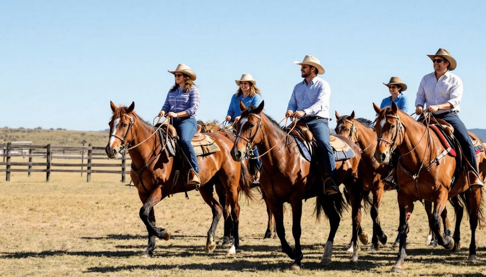 Guests are enjoying a horseback riding activity at a ranch event, guided by an instructor, in a picturesque outdoor setting perfect for private events and company picnics. The scene captures the excitement and camaraderie of participants as they engage in this fun and memorable experience.