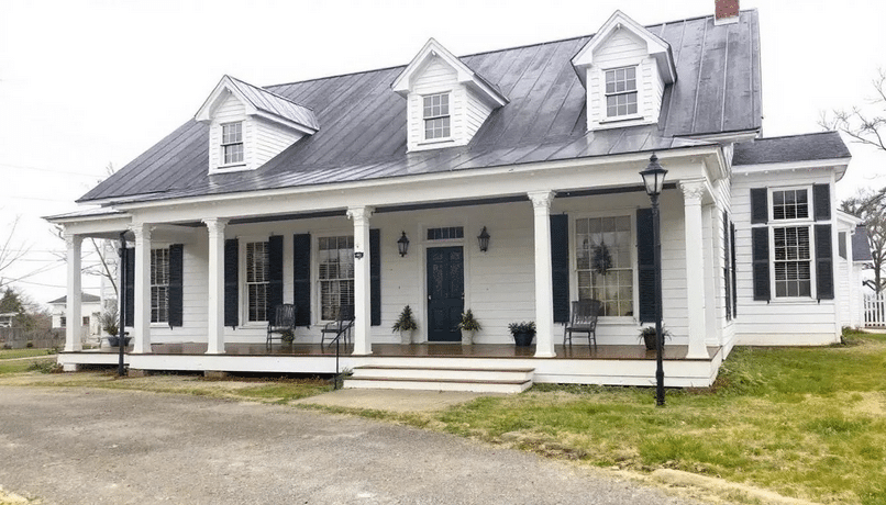 The image depicts a medium-sized plantation style home characterized by its balanced proportions, featuring a welcoming front porch supported by tall columns and charming dormers on the roof. This southern style house plan emphasizes outdoor living spaces with deep overhangs and wraparound porches, making it ideal for family gatherings and entertaining.