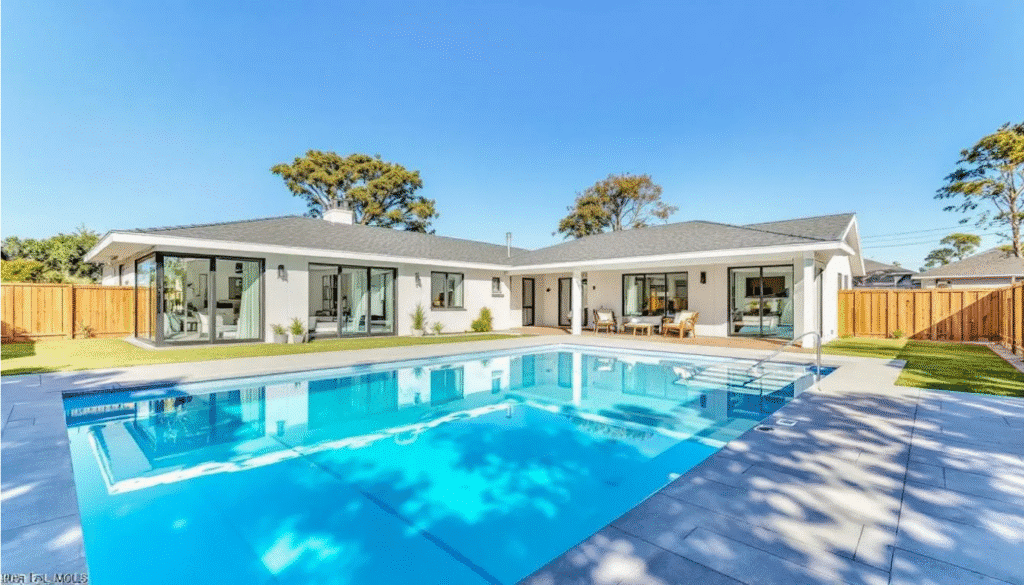 The image depicts a modern ranch style house featuring a spacious great room with large windows that offer views of a sparkling swimming pool just outside. The home includes a well-designed floor plan with a cozy dining area, a functional laundry room, and a welcoming front porch, making it an ideal living space for family gatherings and relaxation.