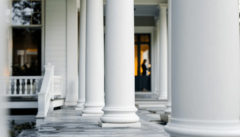 The image showcases a close-up view of tall white columns that support a deep porch typical of plantation style homes, emphasizing the architectural elegance and charm of southern style house plans. The detailed craftsmanship of the columns and the spaciousness of the porch highlight the inviting outdoor living spaces often found in plantation house designs.