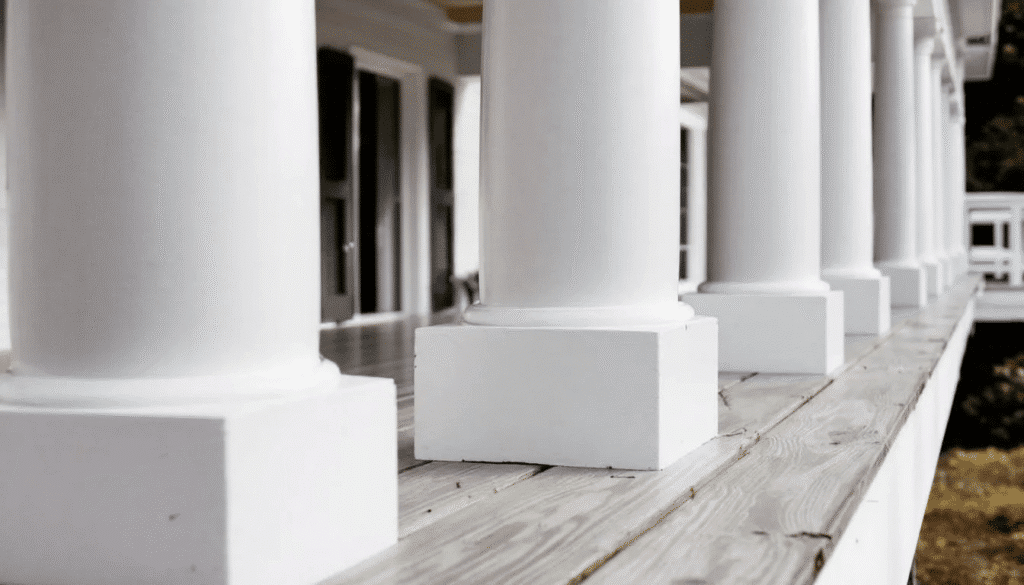 image - Ranch Style Homes USA The image features a close-up view of a wraparound porch adorned with elegant white columns and sturdy wooden decking, embodying the rustic charm of modern farmhouse architecture. This outdoor space highlights the seamless blend of traditional elements and modern functionality, offering a welcoming atmosphere for families to enjoy.