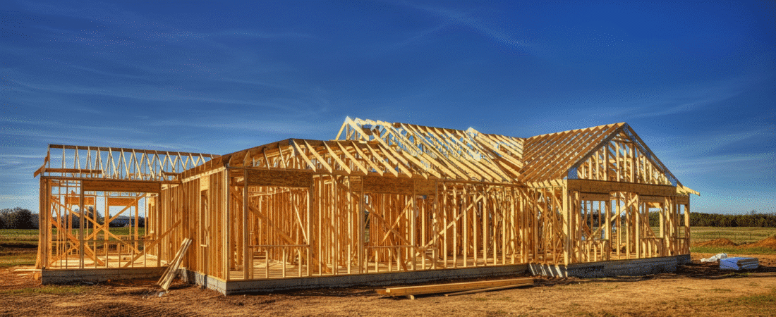 Photograph of a single-family home's wooden frame under construction against a vibrant blue sky, symbolizing new beginnings and future potential in real estate.