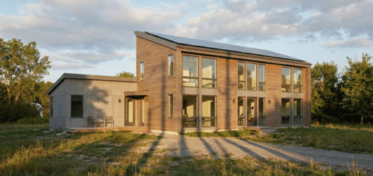 A modern two-story house with large windows, solar panels, surrounded by green grass.